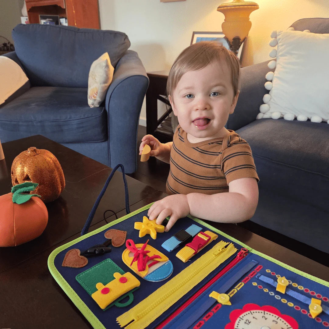 Egy mosolygós kisgyermek önállóan játszik a KalandTáska matatókönyvvel a nappaliban, fejlesztve a finommotorikáját.